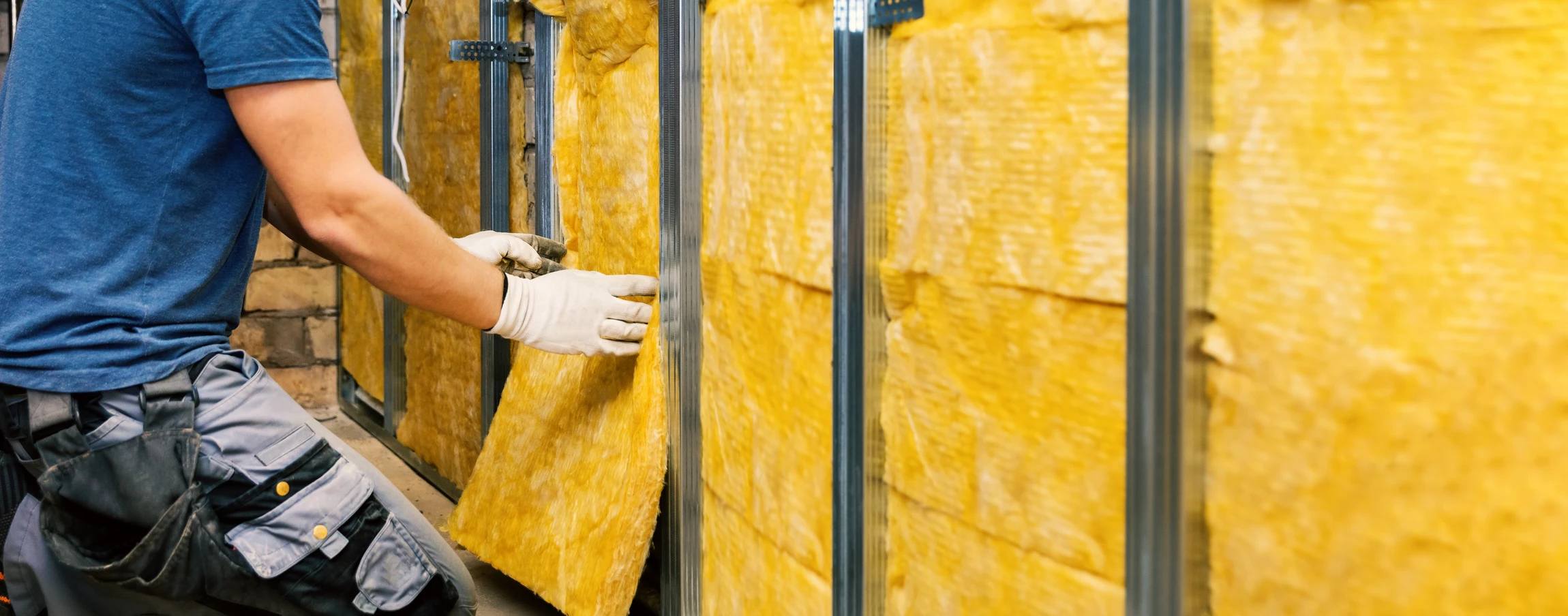 Un professionnel équipé de gants blancs installe de l'isolant thermique jaune en laine minérale entre des montants métalliques dans une cloison intérieure