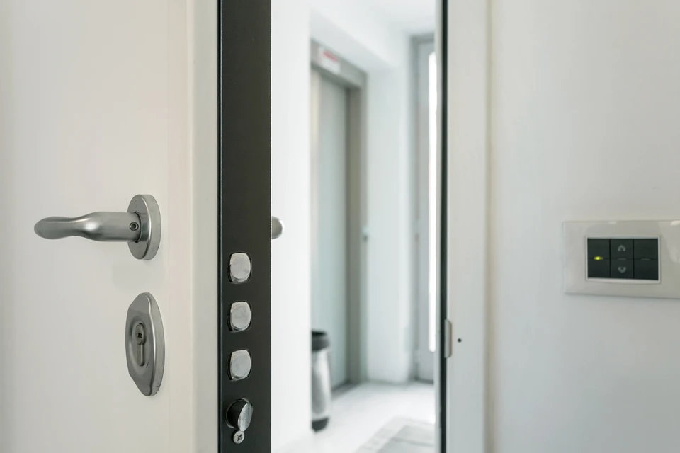 Technicien en salopette rouge et t-shirt blanc installe une serrure sur porte d'entrée en bois foncé dans hall d'immeuble moderne