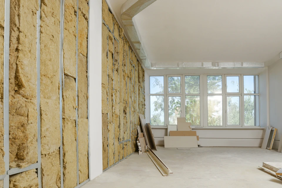 Homme travaillant à genoux sur plancher intérieur, découpant matériau isolant blanc avec cutter